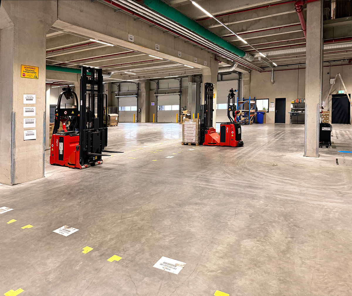 Modernes Lagerhaus mit roten Gabelstaplern und Paletten, das die logistische Abwicklung von Marketing- und Kampagnenprojekten durch Greim Projekt Service veranschaulicht.
