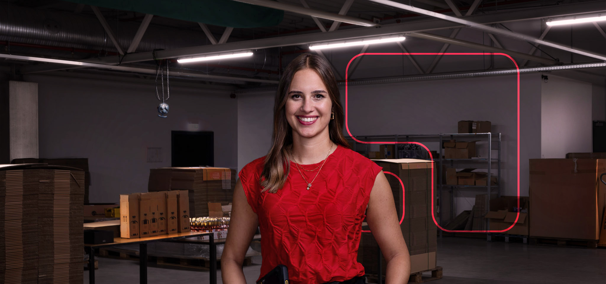 Milena Greim in rotem Oberteil steht in einem Lager mit Kartons und Regalen, symbolisiert die logistische und operative Abwicklung von Marketing- und Promotionsprojekten durch die Greim Projekt Service GmbH.