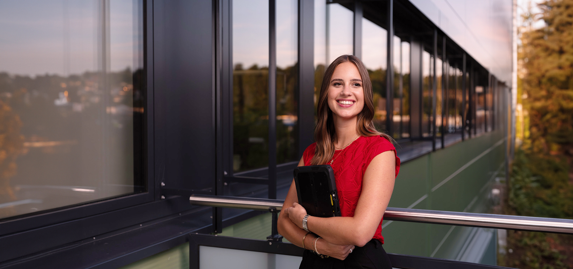 Milena Greim von Greim Projekt Service hält ein Tablet und steht auf einem Balkon eines modernen Bürogebäudes – das Unternehmen begleitet komplexe Marketing- und Promotionsprojekte von der Planung bis zur logistischen Abwicklung.