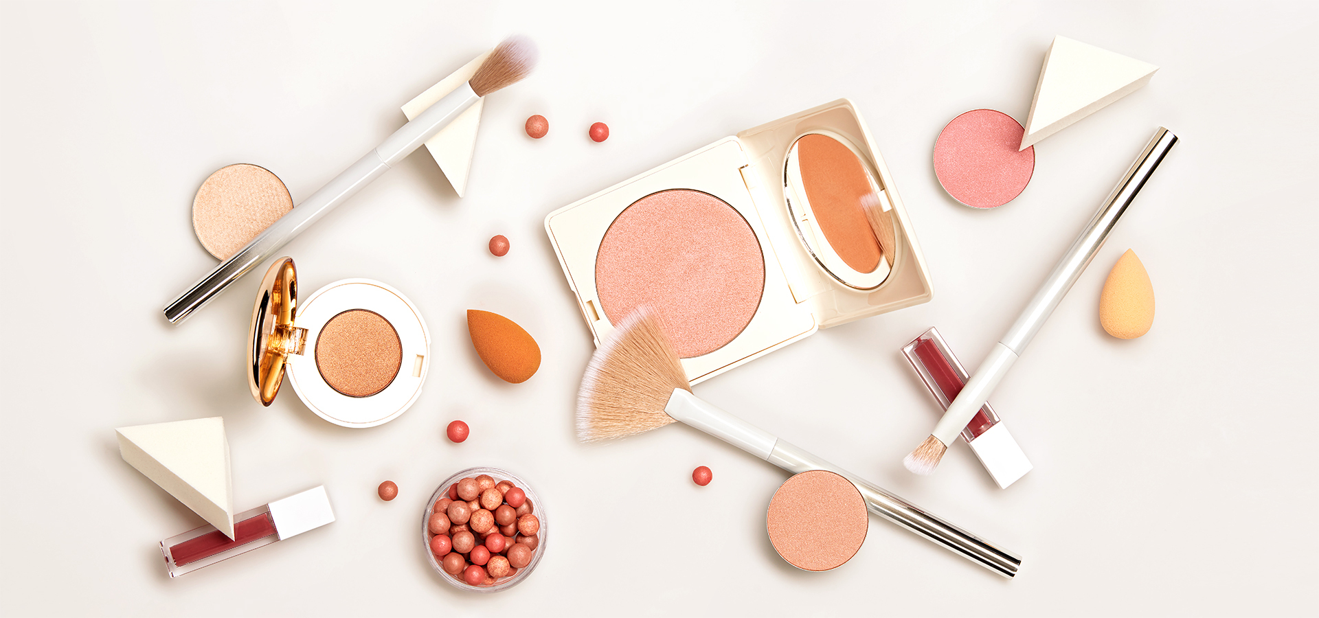 Arrangement von Make-up-Produkten (Puder, Pinsel, Lipgloss, Schwämmchen) auf weißem Hintergrund, passend für Marketing- und Promotionsprojekte von Greim Projekt Service.
